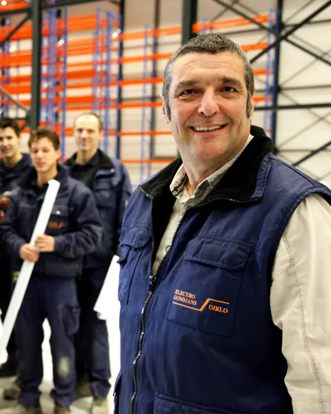 Medewerkers van Electro Gommans in werkkleding in een magazijnhal, vooraan een man met het Electro Gommans-logo op zijn bodywarmer